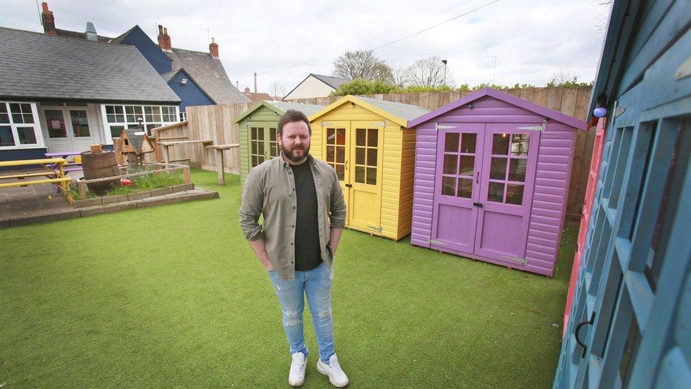 A man stands on a fake green next to a green, yellow, purple, pink and blue huts