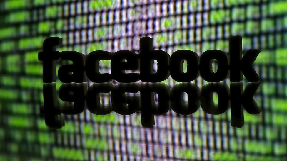 File image showing a 3D prined Facebook logo in front of cyber code displayed on a screen