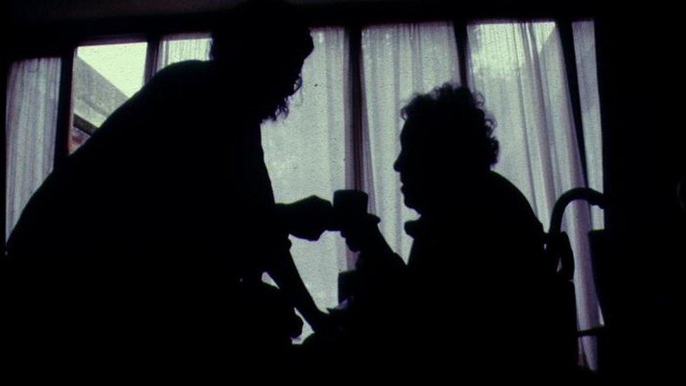 Silhouette of elderly woman being given tea by carer