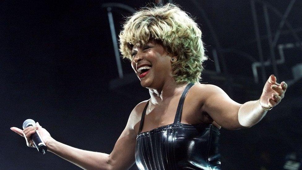 Tina Turner seen smiling with her arms outstretch, microphone in one hand, during a performance in California in 2000