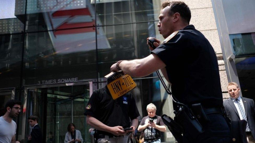 A New York police officer takes away the licence plate of a car that crashed in to pedestrians