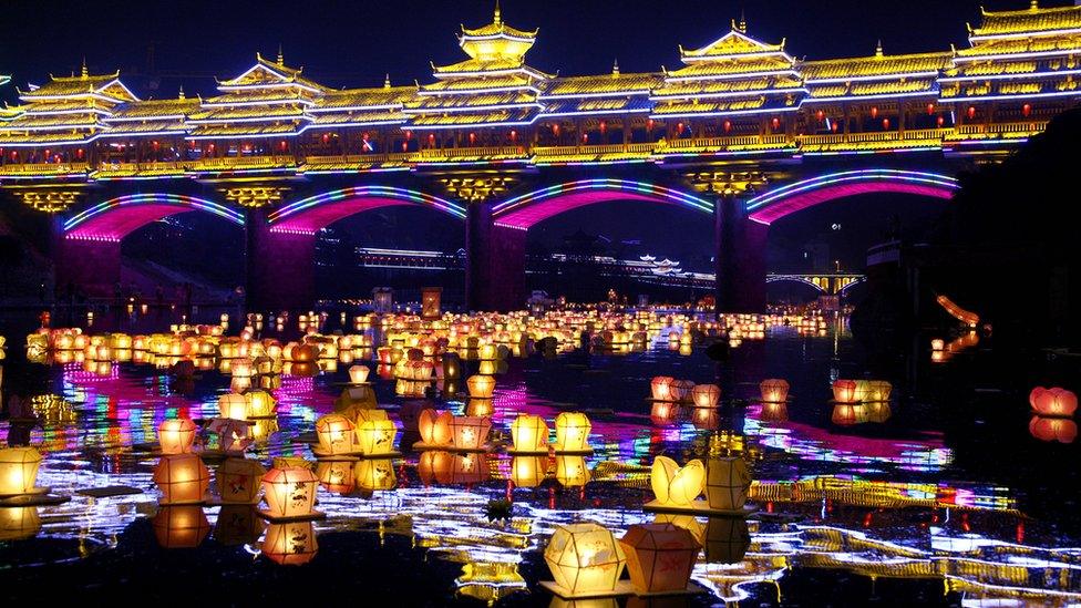 A night scene showing a river covered with hundreds of lanterns, floating under a brightly lit bridge.