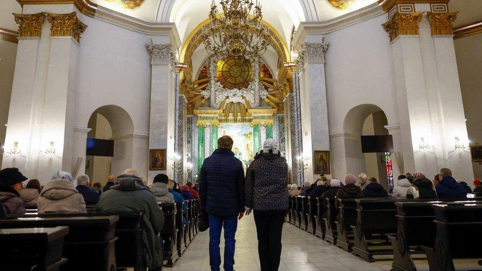 Catholic believer Lesia Shestakova and Orthodox believer Oleksandr Shestakov, who prepare to celebrate Christmas together on the same day for the first time, stand inside the Cathedral of St. Alexander before a service