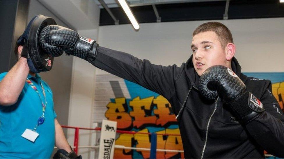 Boy wearing boxing gloves hits a pad being held up by a man