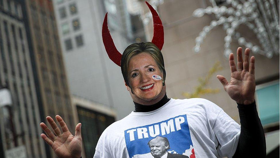 A Trump supporter wearing a Hillary Clinton mask with devil's horns