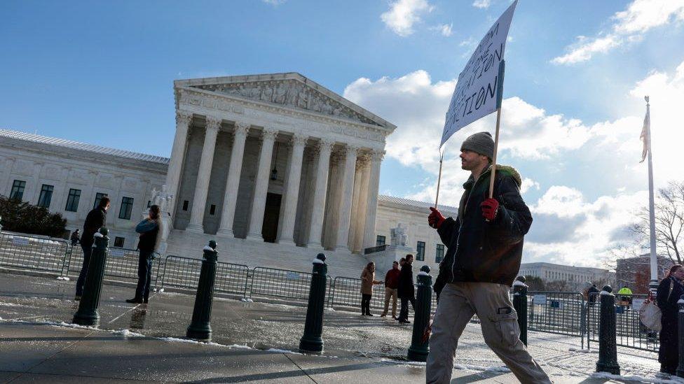 A protester holds a sign that reads "Freedom is one generation from Extinction" as he walks by the US Supreme Court