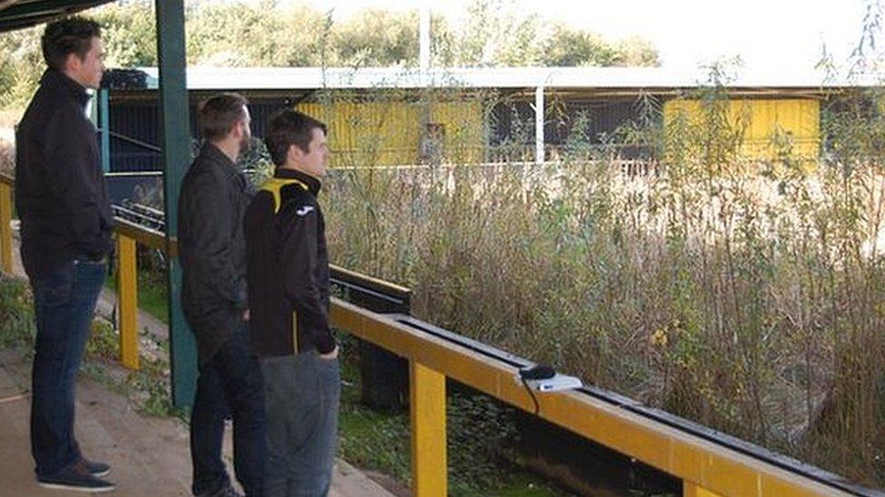 Three fans stand in Meadow Park - Gloucester City's home