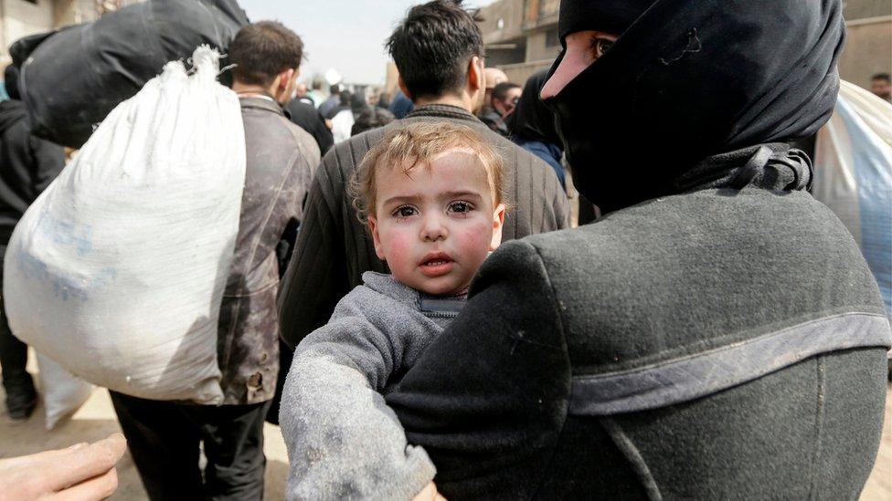 A Syrian woman carrying a child evacuated from the Eastern Ghouta