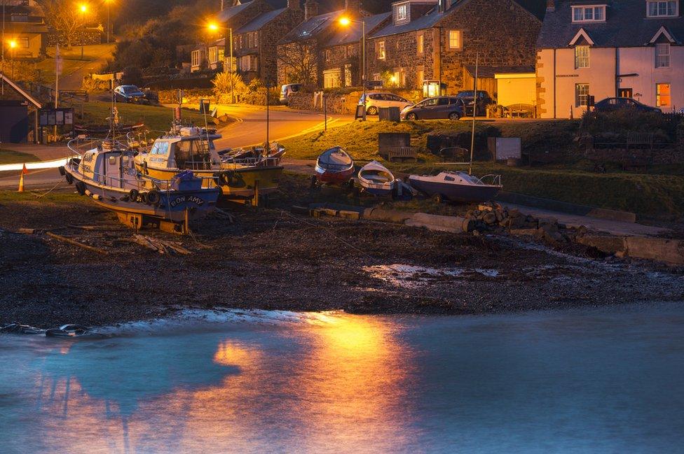 Harbour and boats at dusk with houses and streetlights on behind