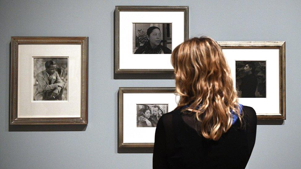 Woman stands in front of a group of photographs at the exhibition