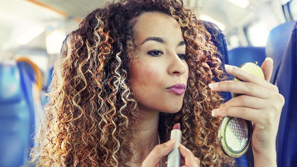 A woman applying lipstick on a train