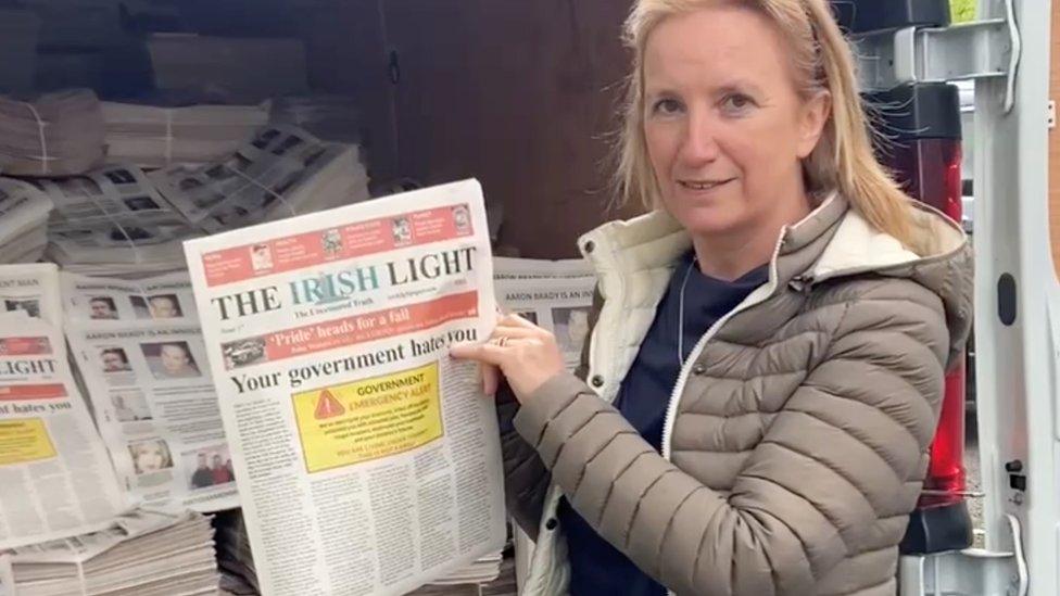 A screengrab of a video showing Gemma O'Doherty wearing a padded jacket as she displays her newspaper from the back of a van