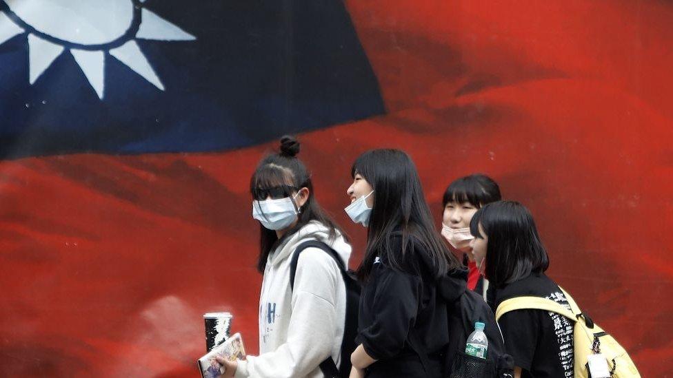 a group of young women walk past taiwan's flag while laughing together