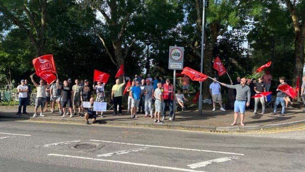 People on a picket line holding red Unite flags