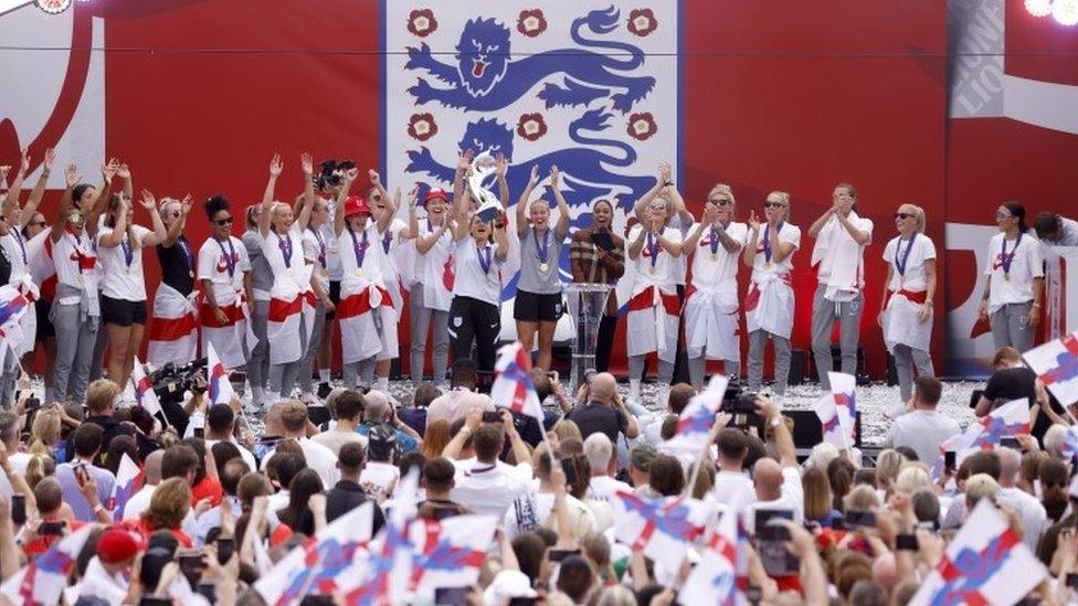 England head coach Sarina Wiegman lifts the trophy on stage during a fan celebration to commemorate England's historic win.