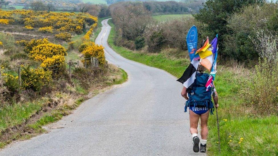 Speedo Mick walking along a road