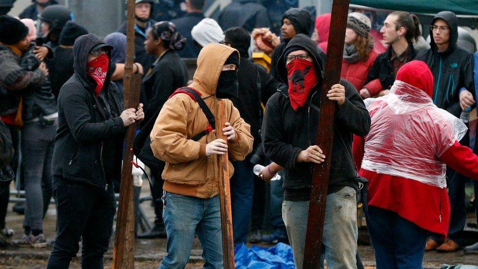 People in masks carrying planks of wood