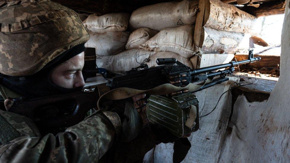 A Ukrainian serviceman points a machine gun through an opening in a sandbag bunker during military exercises