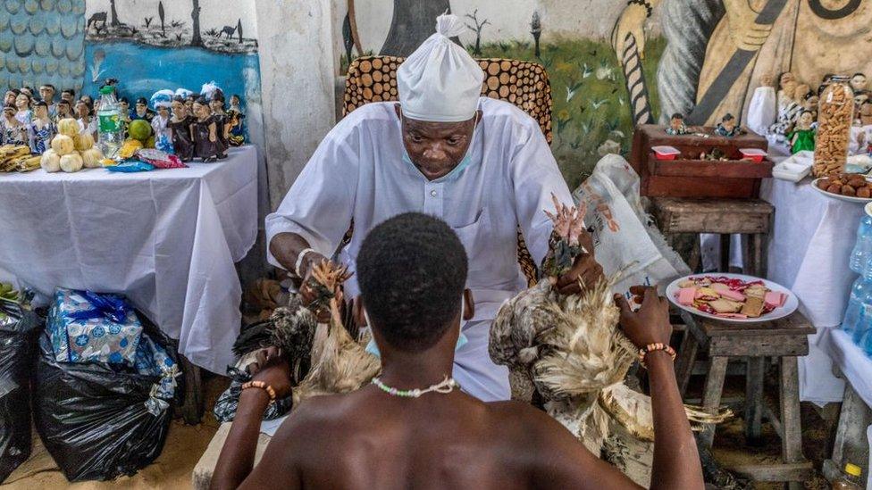 A man kneels before a juju priest