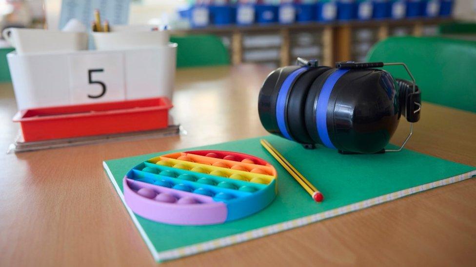 Autism aids, including ear defenders and a fidget spinner, on a pupil's table in a classroom