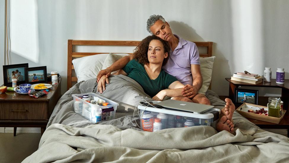 Jennifer Brea and Omar Wasow in bed, surrounded by medication