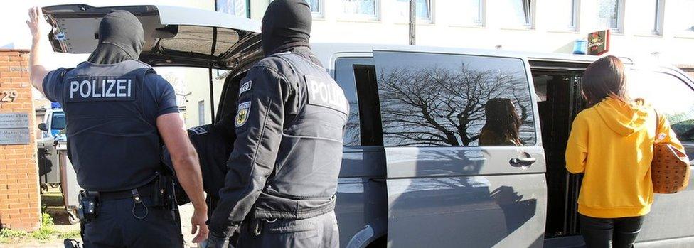 Federal police officers look on as a woman gets into a car during a raid in Hamburg, northern Germany