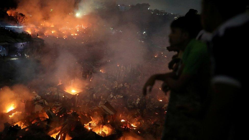 People gather at a rooftop to watch the fire that broke out at a slum in Dhaka, 16 August