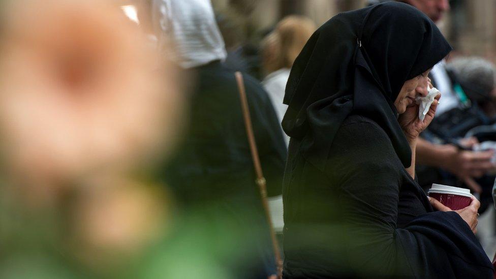 A woman wipes her eye as she looks at flowers in Albert Square