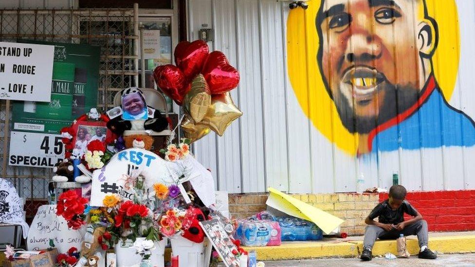 A boy sits next to a makeshift memorial outside the Triple S Food Mart where Alton Sterling was fatally shot by police in Baton Rouge, Louisiana.