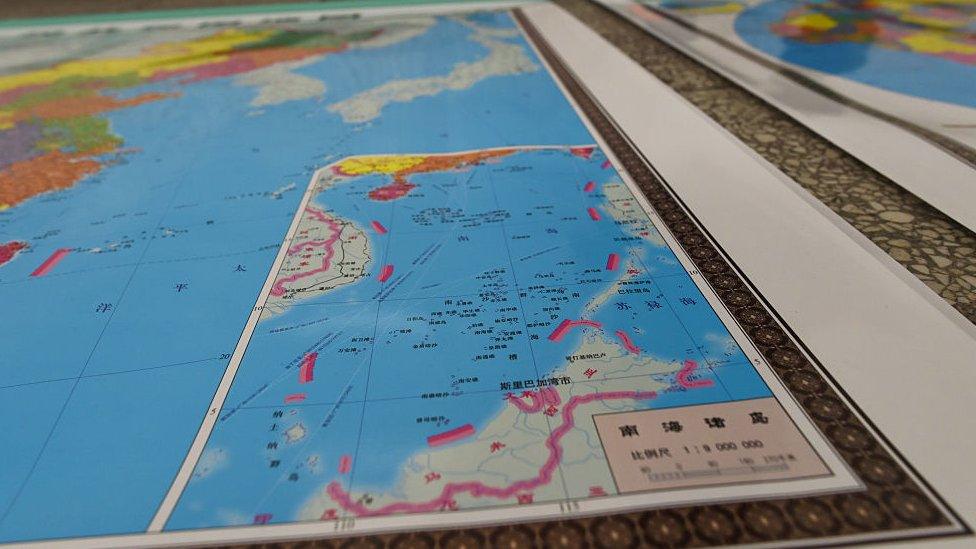 In this photo taken on June 15, 2016 a vendor stands behind a map of China including an insert with red dotted lines showing China's claimed territory in the South China Sea