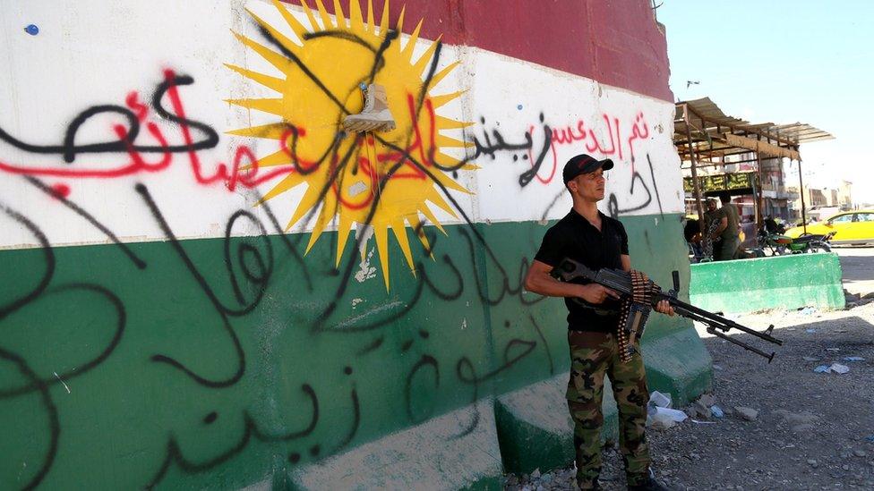 A Shia militiaman stands next to a crossed-out Kurdish flag in Tuz, south of Kirkuk city, Iraq (17 October 2017)