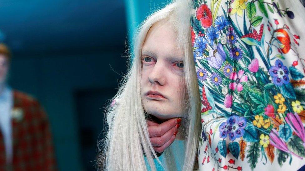 Close-up of female model in floral dress holding a mannequin head that is a replica of her head