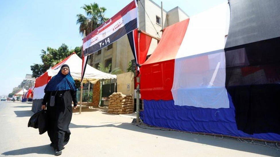 An Egyptian woman walks in front of a polling station covered from outside by Egyptian flags, during the preparations for the upcoming referendum on constitutional amendments in Cairo, Egypt on 18 April 2019