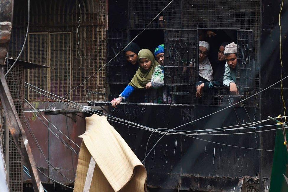 Neighbours watch as National Disaster Response Force and fire brigade personnel carry on rescue work after a building collapsed.