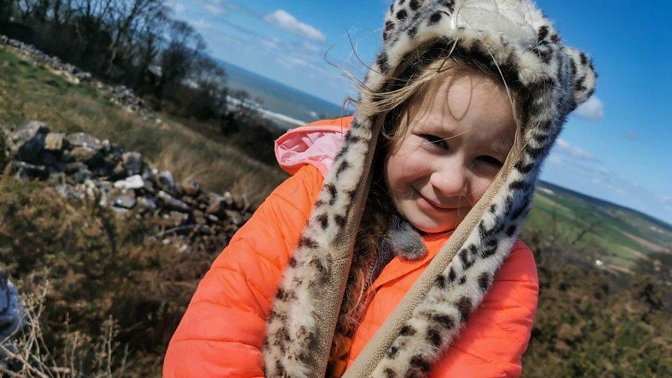 a-young-girl-who-lives-in-an-eco-home-with-her-family-sits-on-a-stone-wall