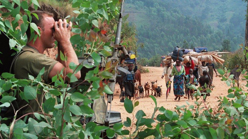 French soldier hidden behind a tree looking through binoculars as Rwandan refugees are heading to the refugee camp of Kivumu, western Rwanda. 12 July 1994