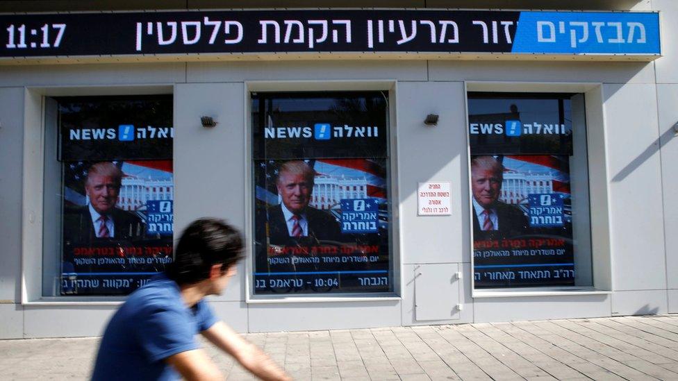 A man cycles past images of Donald Trump displayed on monitors in Tel Aviv, Israel (9 November 2016)