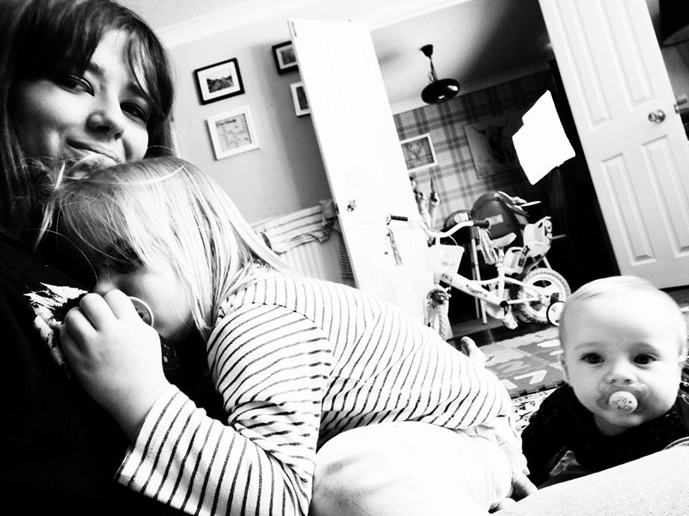 A black-and-white photo of a woman at home with two children