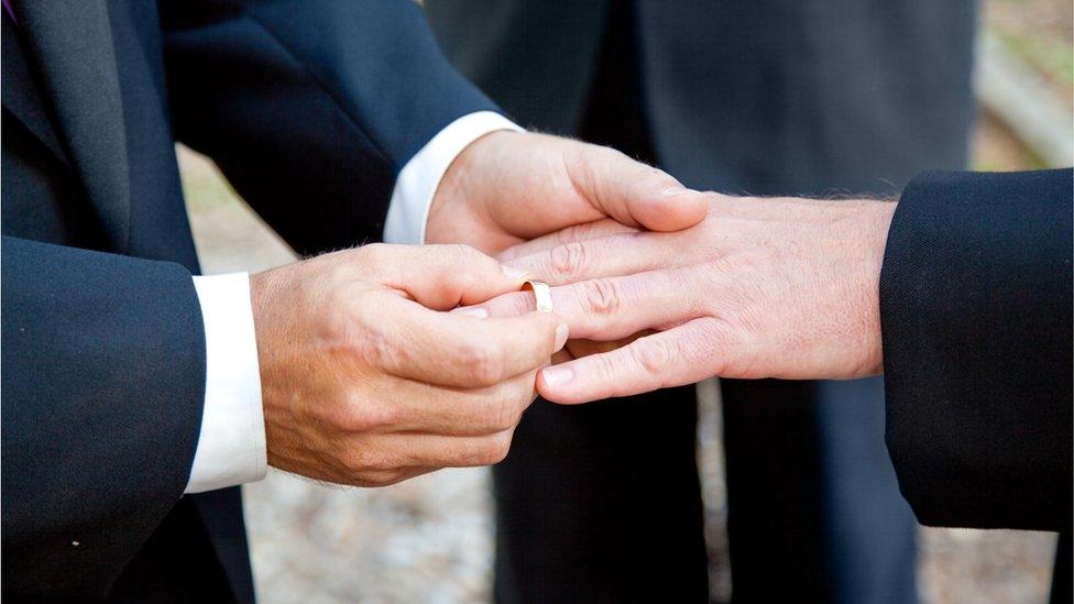 One groom placing a wedding ring on another groom's finger