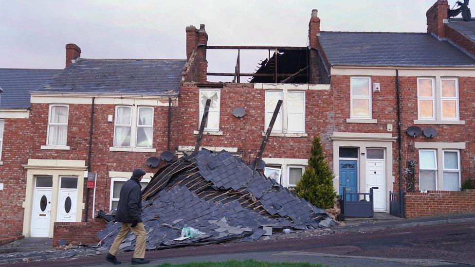 Man walks past house with roof collapsed on ground in front