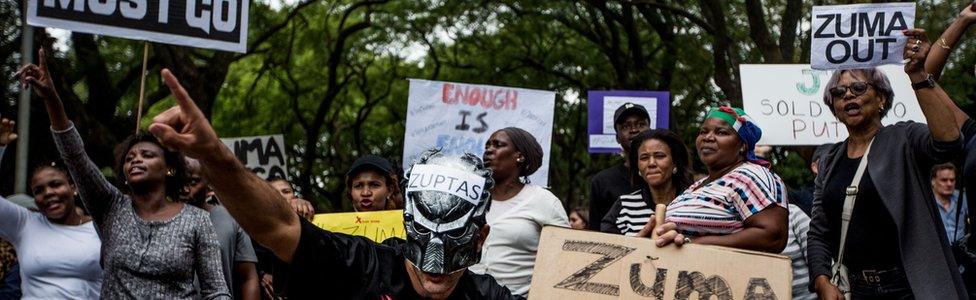 Demonstrators protesting against the South African president and calling for his resignation hold placards and shout slogans outside the Gupta Family compound in Johannesburg on April 7, 2017.