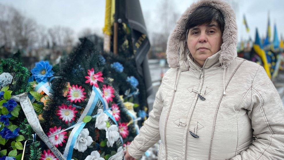 A woman stands next to her son's grave in Cherkasy