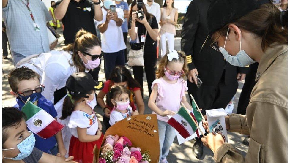 Zara Rutherford in Monterrey being greeted by children who have brought her gifts including flags and flowers