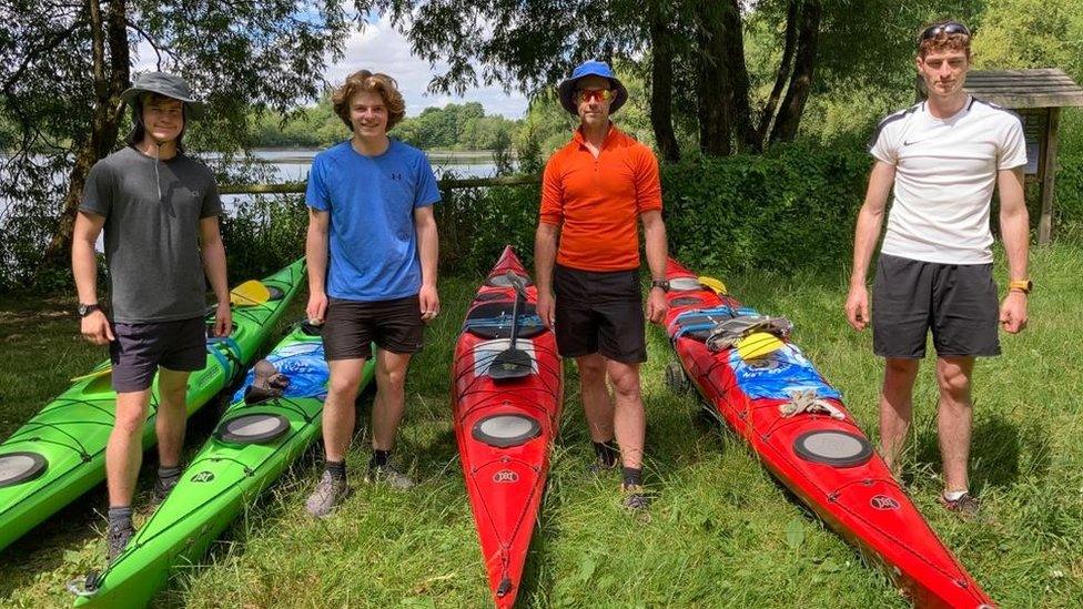 Four males stood beside their kayaks on the grass