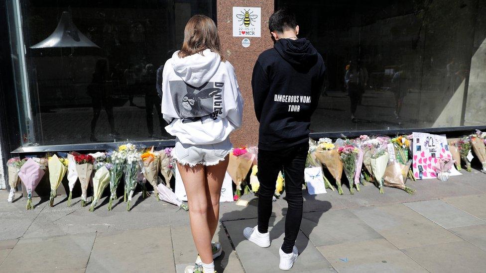 People wearing Ariana Grande sweatshirts look at tributes left in St Anne"s Square on the first anniversary of the Manchester Arena bombing