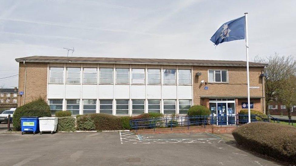 Brick-built two-storey police station with flag flying and car park