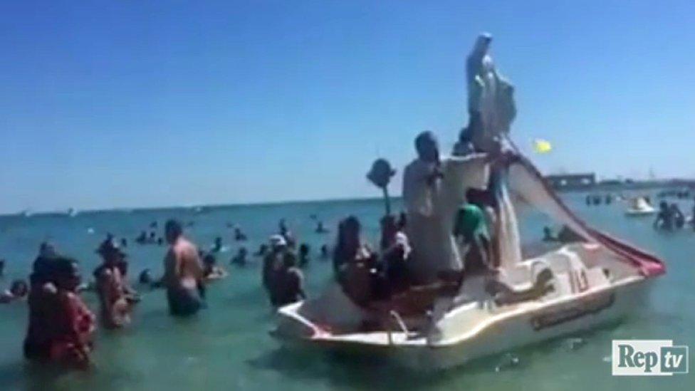 A priest blesses bathers from the back of a seaside pedalo