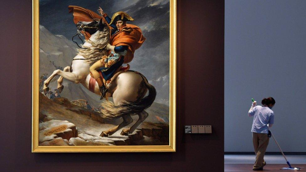 A cleaner mops the floor next to the painting titled "Napoleon Bonaparte, First Consul, Crossing the Alps" by French artist Jacques-Louis David at the Louvre Abu Dhabi Museum during a media tour on November 6, 2017 prior to the official opening of the museum on Saadiyat island in the Emirati capital on November 8.