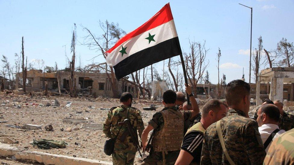 Forces loyal to Syrian President Bashar al-Assad hold up a Syrian flag as they walk through a recaptured military complex in Aleppo (5 September 2016)