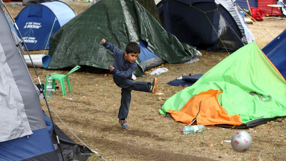 A boy kicks a ball next to tents at the Traiskirchen camp